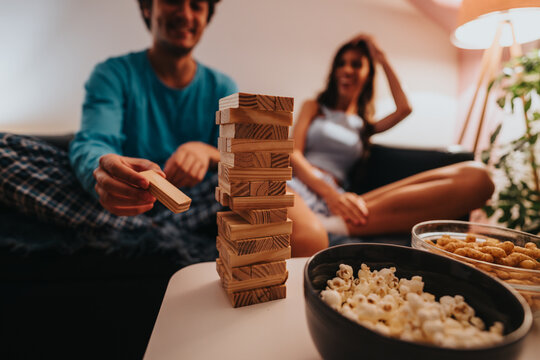 Two friends are having a relaxing game night at home, enjoying Jenga and delicious snacks. The atmosphere is casual and filled with laughter, highlighting a cozy and enjoyable evening together. - Powered by Adobe