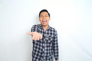 Fototapeta premium carefree asian man presenting hand with laughing expression showing joy and playful emotion wearing casual plaid shirt isolated on white background