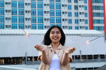 carefree asian young woman holding sparkler celebrate new year eve with laugh and dance in rooftop apartment outdoor with city building background