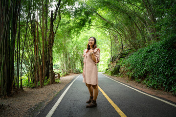 Fototapeta premium A woman stands in the middle of a road on a mountain green season in the forest.