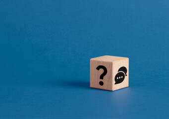 Question mark and speech bubble symbols on wooden cube on blue background