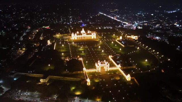 Aerial view of Mysuru Palace illuminated at night, surrounded by sparkling city lights. Highlights the grandeur and cultural richness of Karnataka's iconic royal landmark. India.