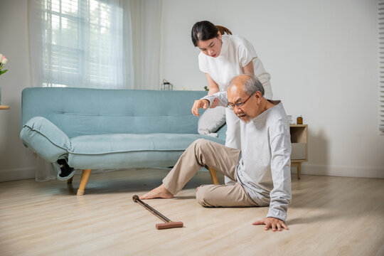 Asia young woman halping her father after falling down on floor, elderly old man with walking stick fall on ground and daughter camp to help at home in living room, family health care