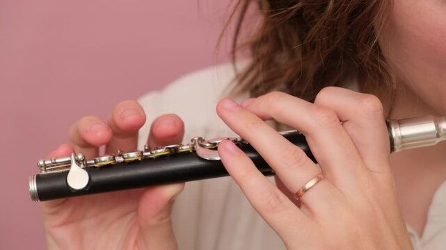 Hands holding a piccolo flute against a pink background. Close-up video for music and instrumental design concepts