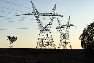 Silhouette of power lines and power poles with high voltage electricity at sunset