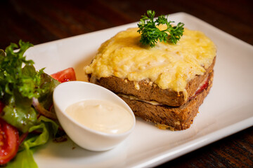 A plate of food featuring a sandwich topped with scramble egg and parsley, served with a side of...
