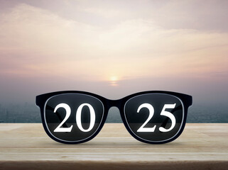 2025 white text with black eye glasses on wooden table over city tower and skyscraper at sunset,...