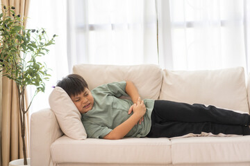 Portrait of sick unhappy little child asian boy touching belly stomach with suffering from stomach...
