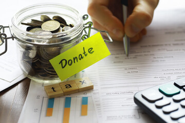 Charity Donation Planning: Jar of Coins, Tax Forms, Calculator, and Hand Writing on Document