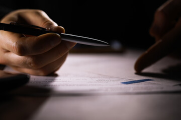 Close-up of Hands Reviewing and Signing Documents in Low Light Office Environment