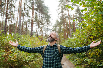 Handsome man standing in the middle of nature with open arms and closed eyes. Peaceful atmosphere...