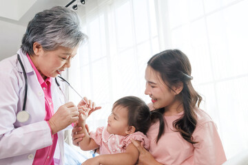 Happy senior female pediatrician professional doctor talk and play to asian girl sitting on mother before exam treatment at hospital or clinic. asia medical child health care.