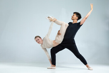 Professional International Sportive Couple of Asian Man and Caucasian Woman Performing As Ballet Dancers Over Grey in Studio During Suppots in Classical Dance Choreography. © danmorgan12