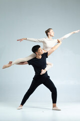 Professional International Sportive Couple of Asian Man and Caucasian Woman Performing As Ballet Dancers Over Grey in Studio During Suppots in Classical Dance Choreography. © danmorgan12