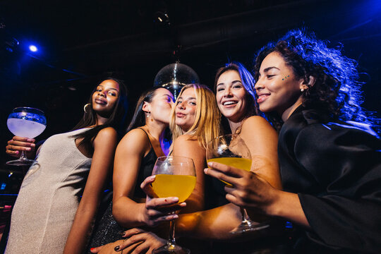 A cheerful group of friends having fun during a night out at a lively nightclub, holding drinks and dancing the festive atmosphere.