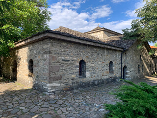 The historic ossuary church Sveta Nedelya in Batak, a stone-built structure with arched windows and a tiled roof, surrounded by a cobblestone pathway and greenery.