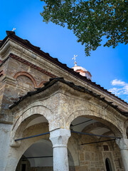 The facade of Saint Nikola Church in Dryanovo, Bulgaria, displays rustic stone arches and intricate brickwork, with a cross-topped dome peeking above the roofline.