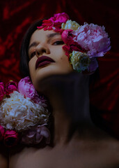 Portrait of a woman with her face surrounded by flowers, with dark lipstick in a dark tone