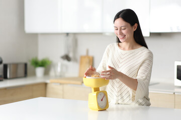 Happy asian woman weighing food in the kitchen