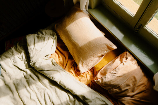 Unmade bed with crumpled sheets and sunlight coming in through the window