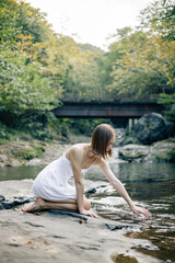 Fototapeta premium A tranquil young woman sitting calmly by the river while wearing a lovely summer dress
