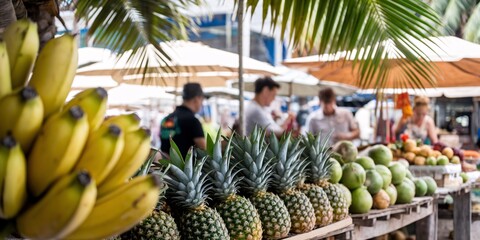 Obraz premium Vibrant image showcasing a variety of fresh tropical fruits - bananas, pineapples, and coconuts - displayed at an outdoor market stall with a shallow depth of field. 