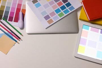 Designer's workplace with tablet, laptop, palettes and stationery on white table, flat lay