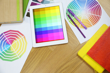Designer's workplace with tablet, palettes and stationery on wooden table, flat lay