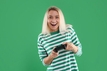 Fototapeta premium Happy woman playing video games with controller on green background