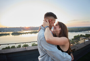 A couple shares a tender moment on a rooftop, their silhouettes etched against the evening sky.