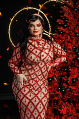 A beautiful young girl plus size model in a red evening dress with bright makeup with a snake. New Year's photo shoot with a snake