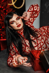 A beautiful young girl plus size model in a red evening dress with bright makeup with a snake. New Year's photo shoot with a snake