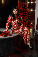 A beautiful young girl plus size model in a red evening dress with bright makeup with a snake. New Year's photo shoot with a snake