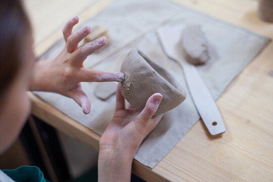 Close up of girl's hands sculpting cup from clay. Children's workshop at pottery studio. Creating ceramics with own hands. Selective focus.