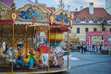 Fototapeta premium Enchanting carousel at a festive Christmas market, surrounded by charming European architecture and holiday spirit. Perfect for winter holidays, family fun, and travel themes. Sibiu, Romania