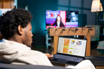 Self employed man working in personal office, checking statistical data financial graphs on laptop screen. Remote employee in living room comparing business graphic economic figures