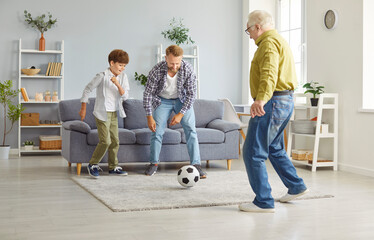 Happy little child boy playing football game with elderly senior grandfather and young smiling...