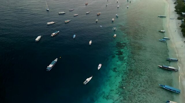 Aerial view of boats on the clear water of the serene sea with a beautiful tropical coastline, Gilli Trawangan, Indonesia.