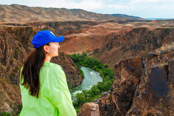 Young woman traveler standing against the Black Canyon landscape. The Black Canyon is part of the Charyn Canyon and Charyn National Park. Located in the Almaty region in south-eastern Kazakhstan