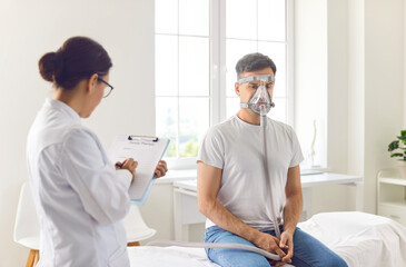 Man is inhaling oxygen through a mask during a visit with a doctor and nurse in a hospital. His...