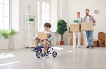 Son joyfully riding a tricycle, celebrating the family relocation or move to a new home or real...