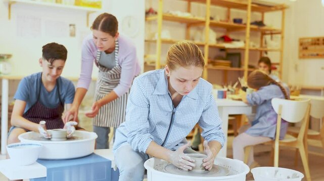 Pleased underage attendees of pottery circle working at throwing-wheel with female instructor