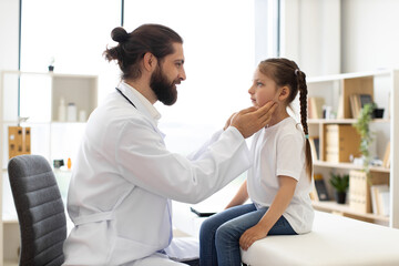 Obraz premium Caucasian male doctor examines throat of young girl in clinical setting. Doctor checks for enlarged lymph nodes and health issues. Scene captures concept of healthcare, medical diagnosis.