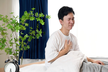寝室で胸を抑えて苦しむ若いアジア人男性