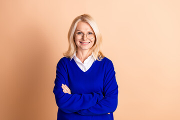 Elegant mature woman in blue sweater smiles confidently against beige background showcasing timeless style and sophistication
