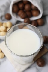 Glass of macadamia milk and nuts on white marble table, closeup