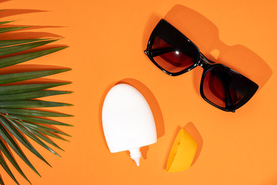 Sun protection essentials with sunglasses and lotion on orange
