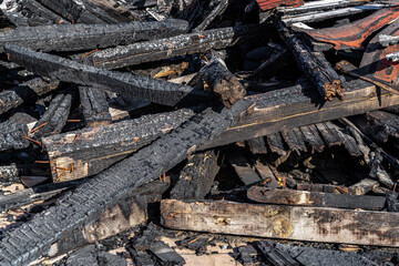 Heap of charred wooden boards after the fire. Pile of burnt wood planks on a sunny day. Fire accident and coals concept. Wooden board became black by heat and fire.