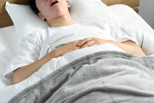 ベッドの上で口を開けて寝るアジア人男性