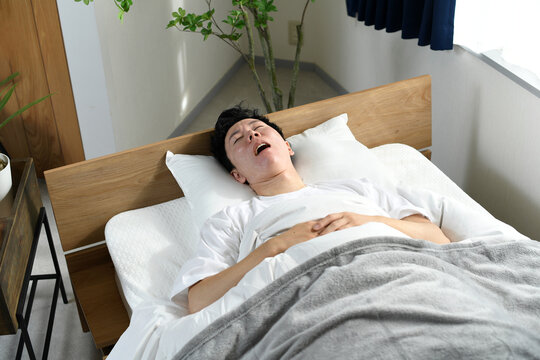 ベッドの上で口を開けて寝るアジア人男性